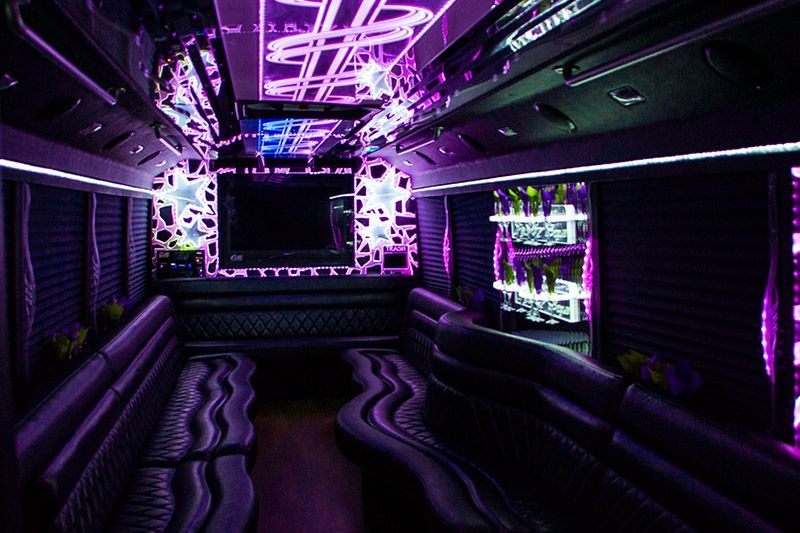 Neon purple-lit luxury limousine interior with black leather seating and a glowing TV screen