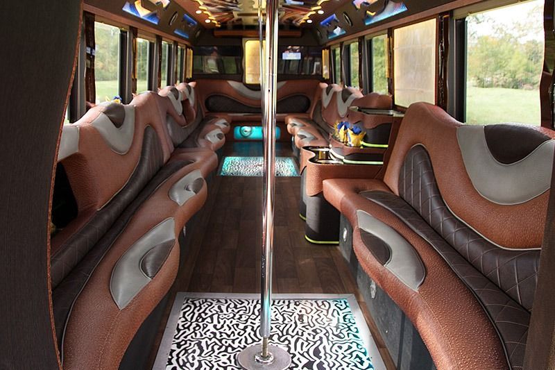 Interior of a luxury bus with brown seats, patterned floor, and a central pole in the aisle.