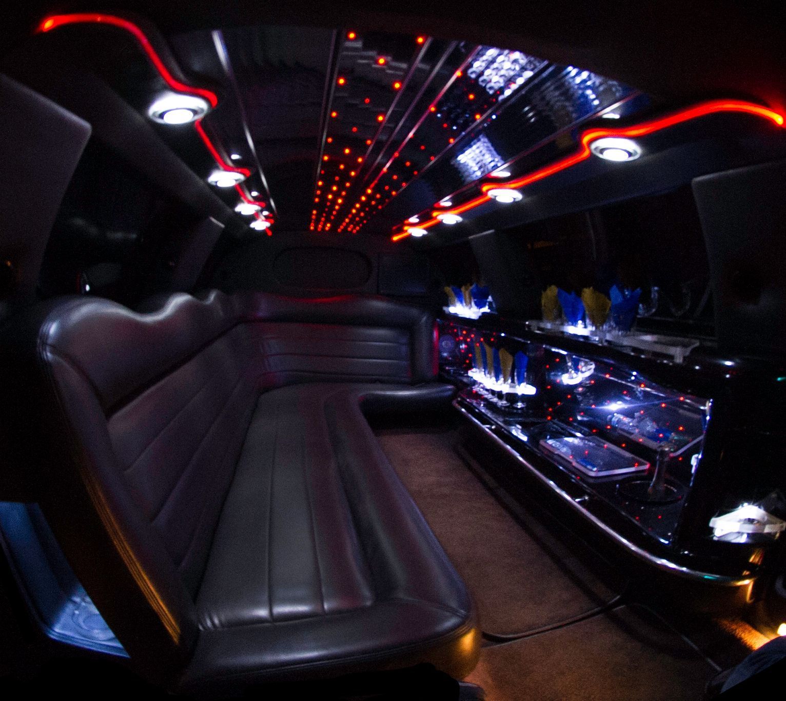 Luxury limo interior with black leather seats, red LED ceiling lights, and a mirrored bar counter