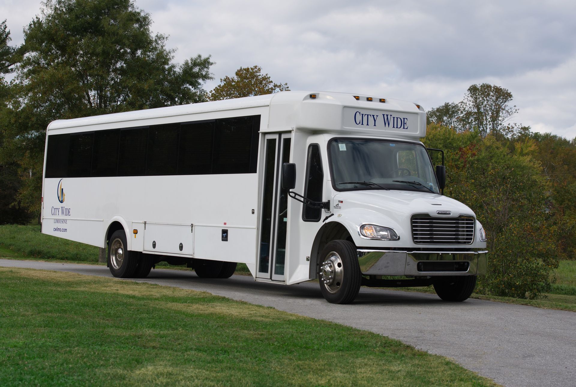 White city bus parked on a road beside grass and trees