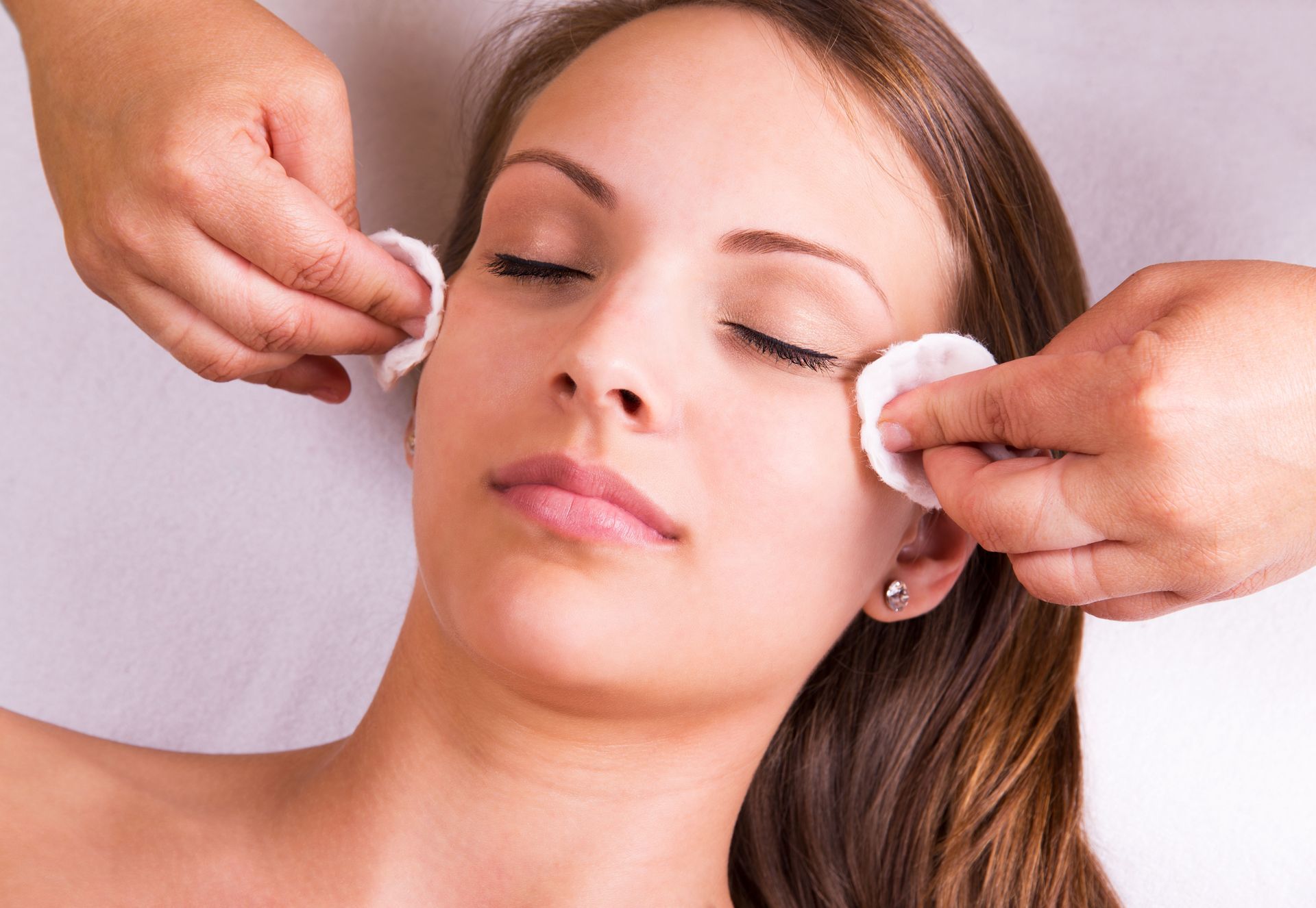 Person receiving a facial treatment as cotton pads wipe their closed eyes