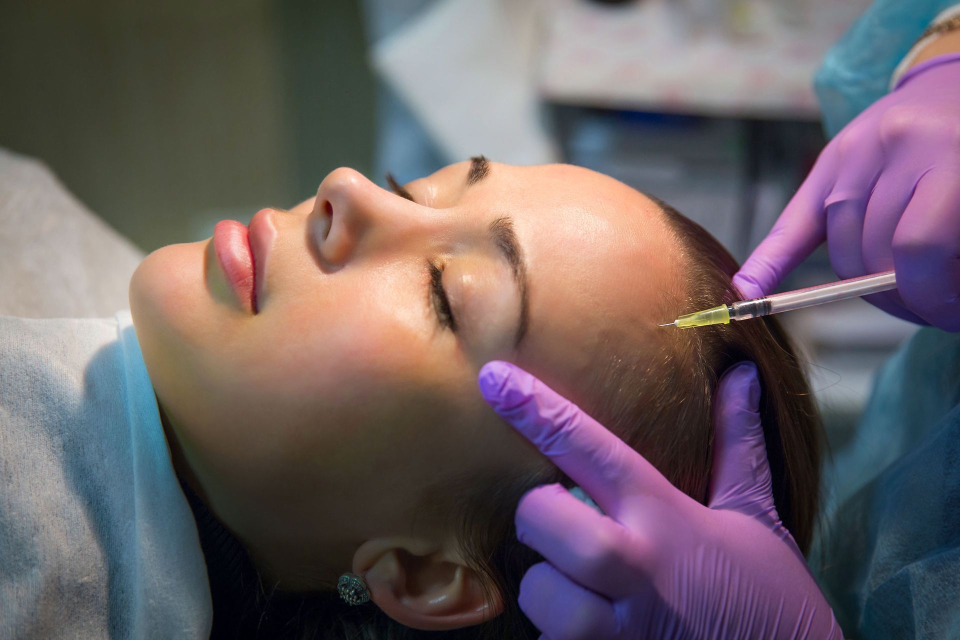 Cosmetic treatment on a woman’s forehead with purple-gloved hands and a syringe.