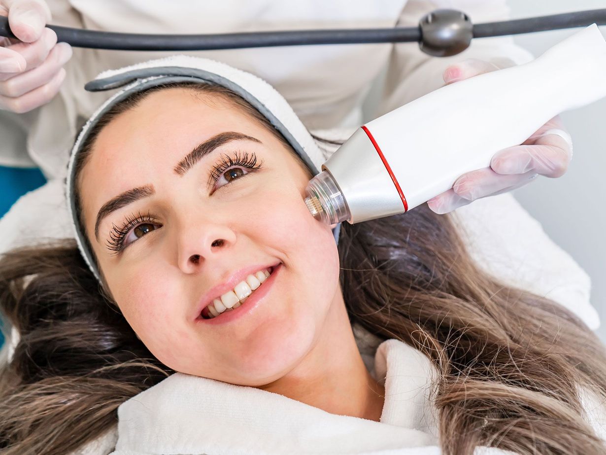 Facial spa treatment with a woman smiling as a gloved hand uses a handheld device on her cheek