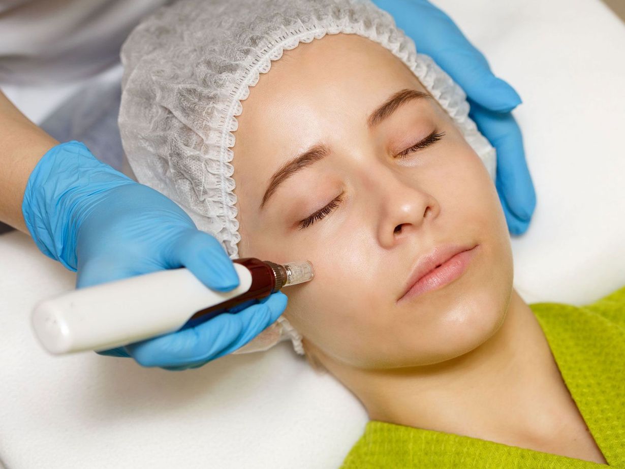Cosmetic facial treatment with gloved hands using a wand on a woman wearing a hair cap