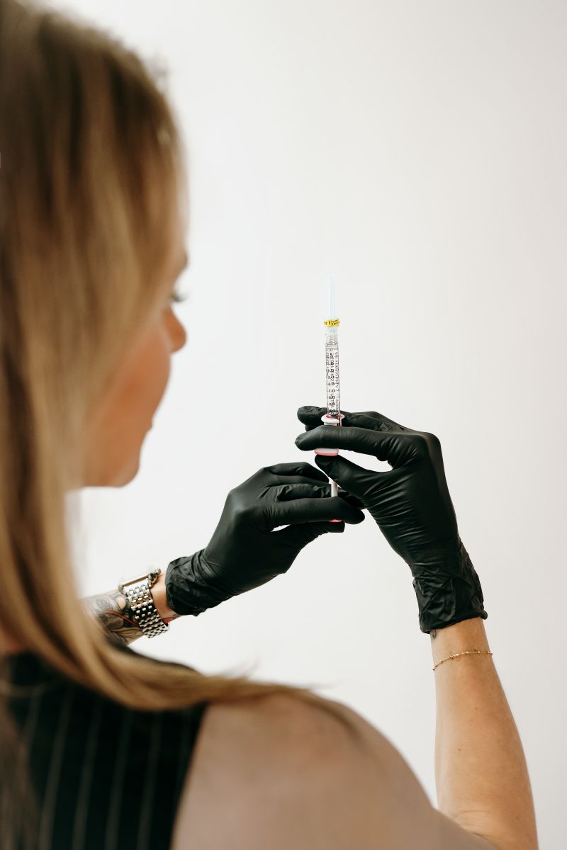 Gloved hands holding a syringe upright, preparing for an injection against a plain white background