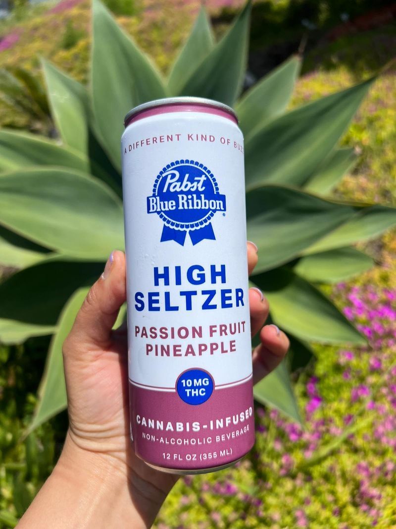 A person is holding a can of pabst blue ribbon high seltzer passion fruit pineapple