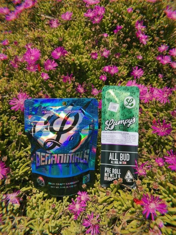 A bag of weed and a bottle of weed are sitting in a field of flowers.