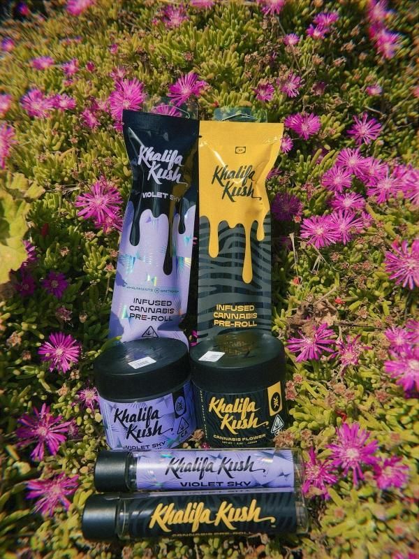 A bunch of khalifa kush products are sitting in a field of purple flowers.