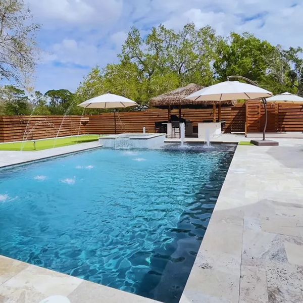 Modern backyard pool with turquoise water, white umbrellas, lounge chairs, and wooden privacy fence