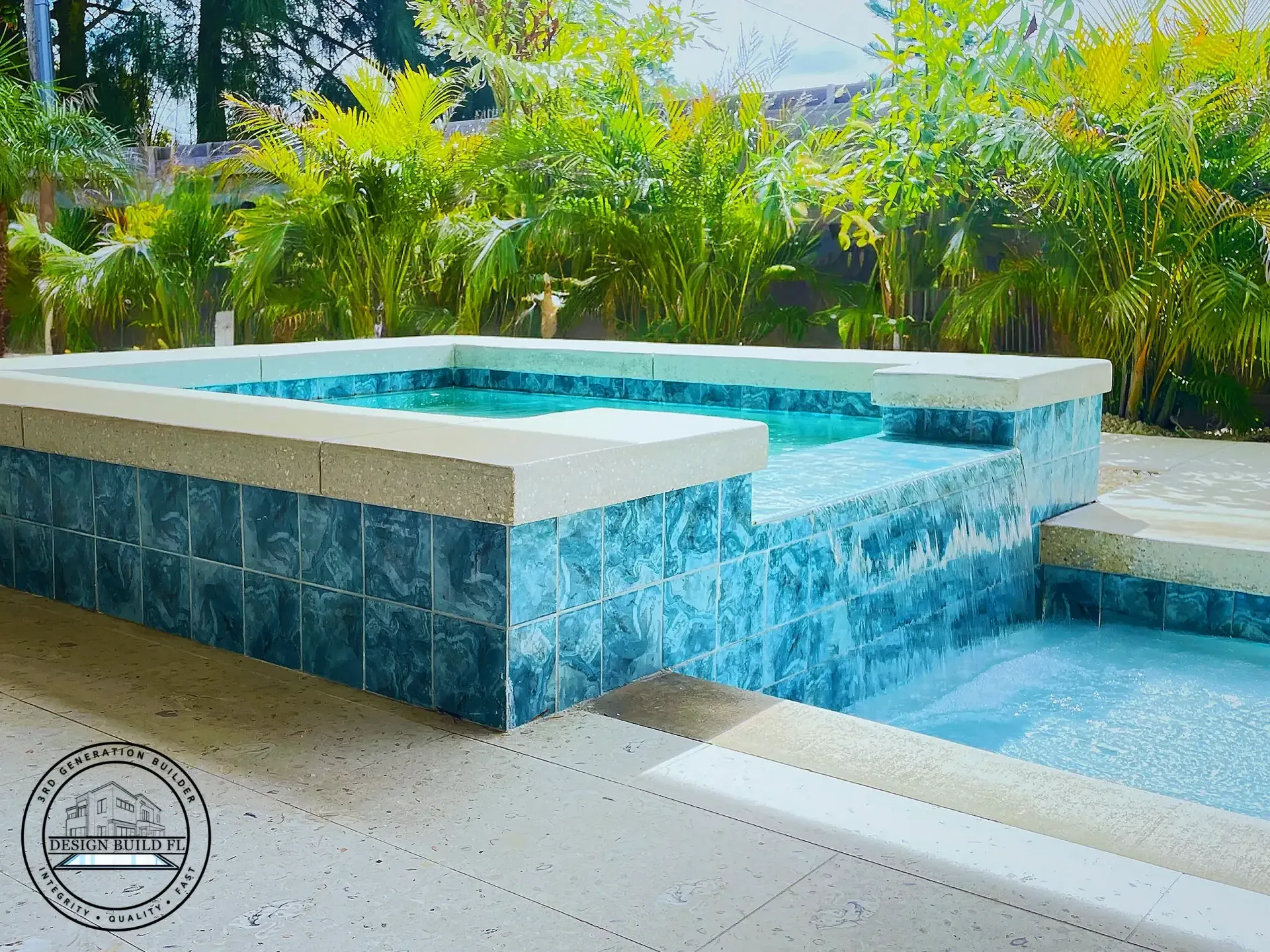 Blue-tiled backyard spa with bubbling water, surrounded by lush tropical plants and a stone patio.