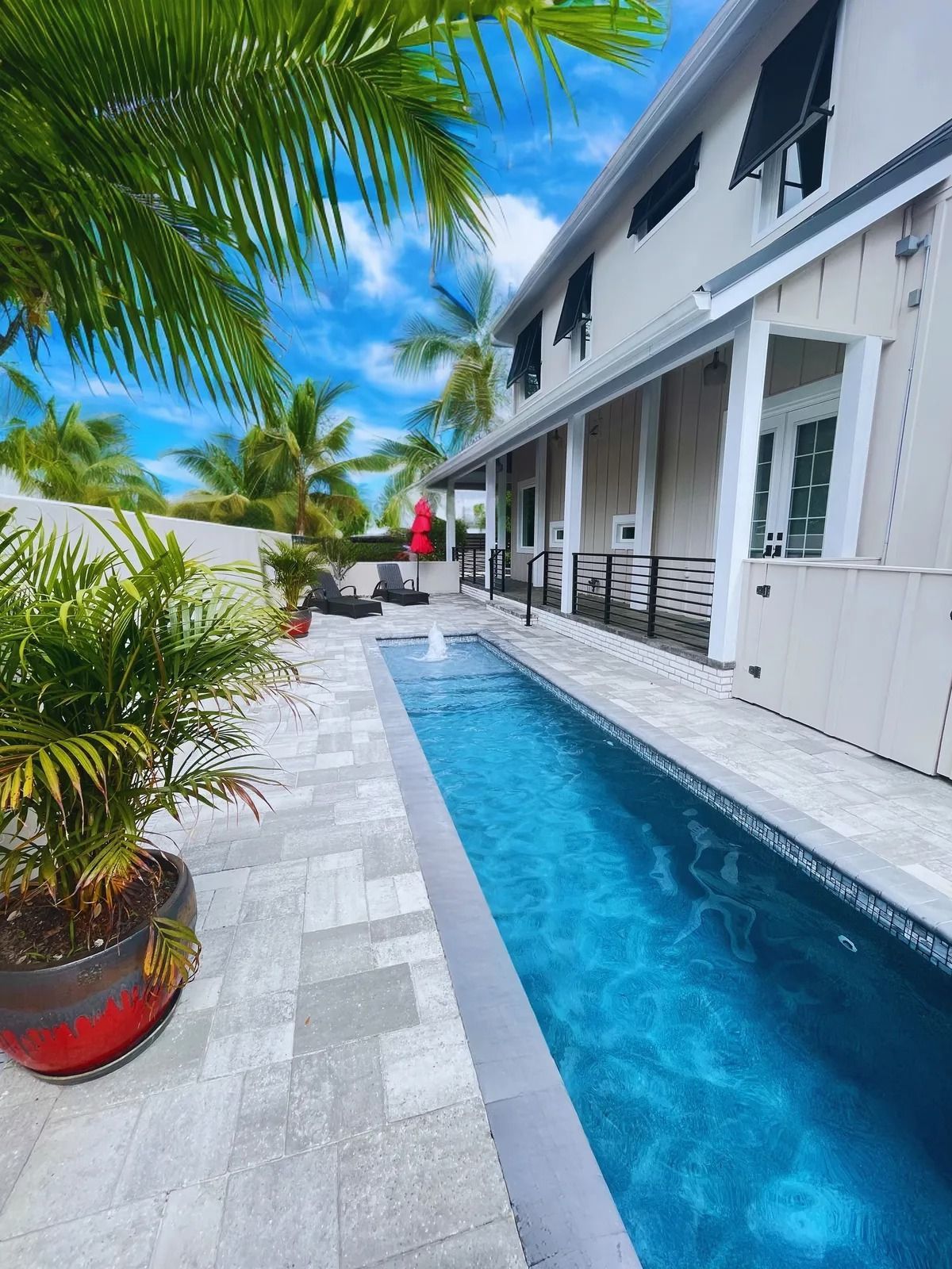 Tropical courtyard with a narrow blue pool beside a white building and palm trees