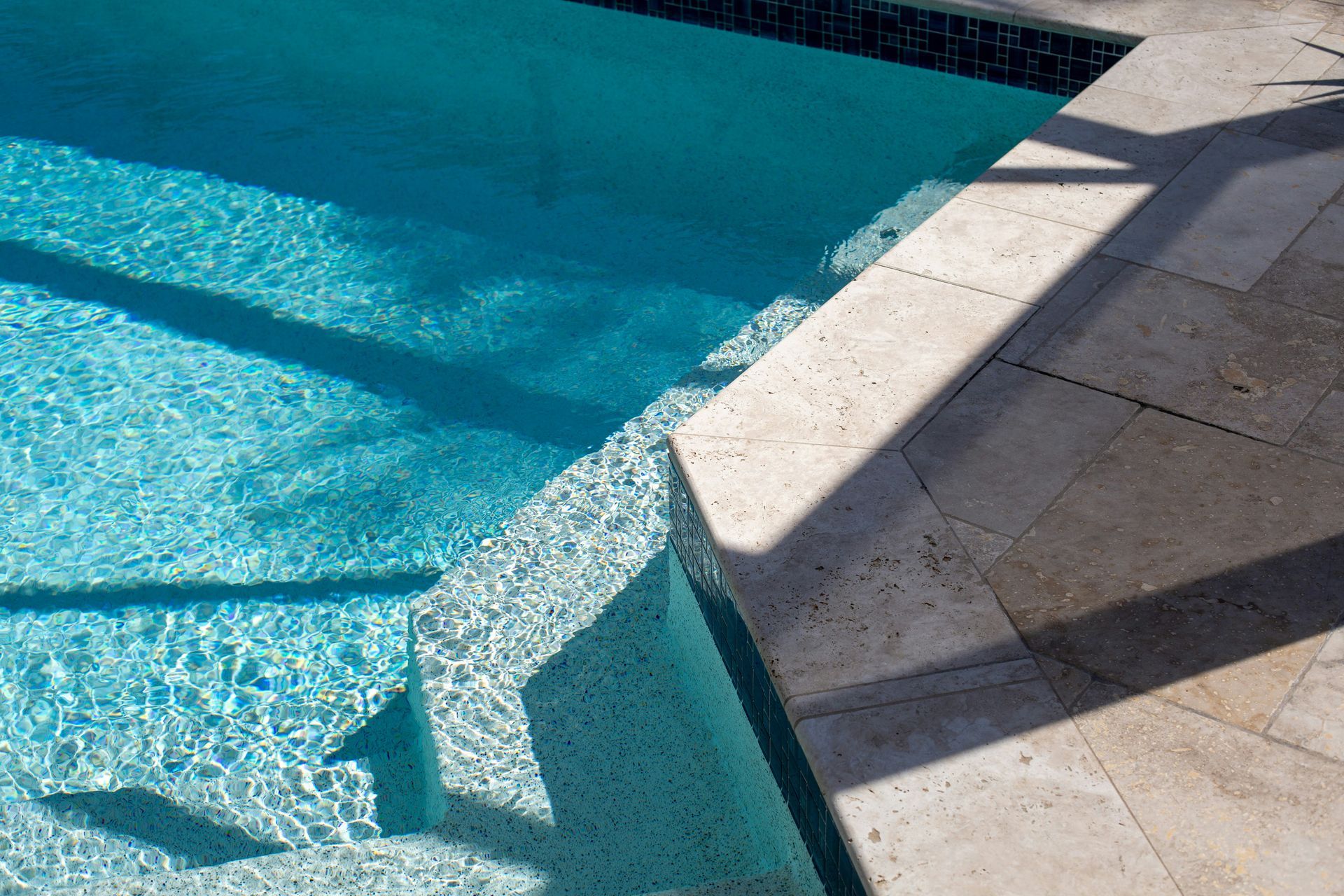 Sunlit swimming pool edge with blue water and stone deck shadows