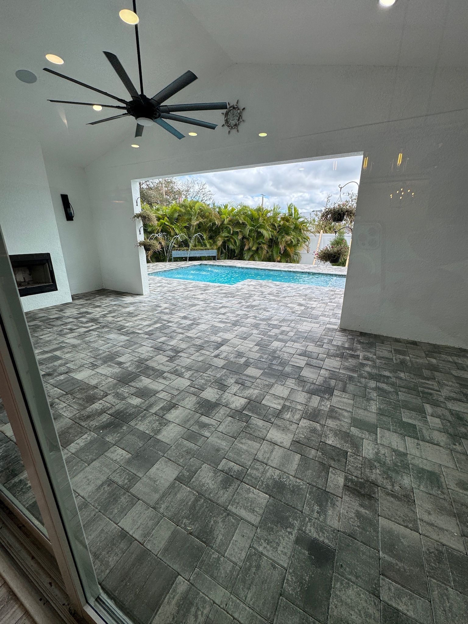 Covered patio with gray tile floor, ceiling fan, and open view to a blue pool and tropical greenery