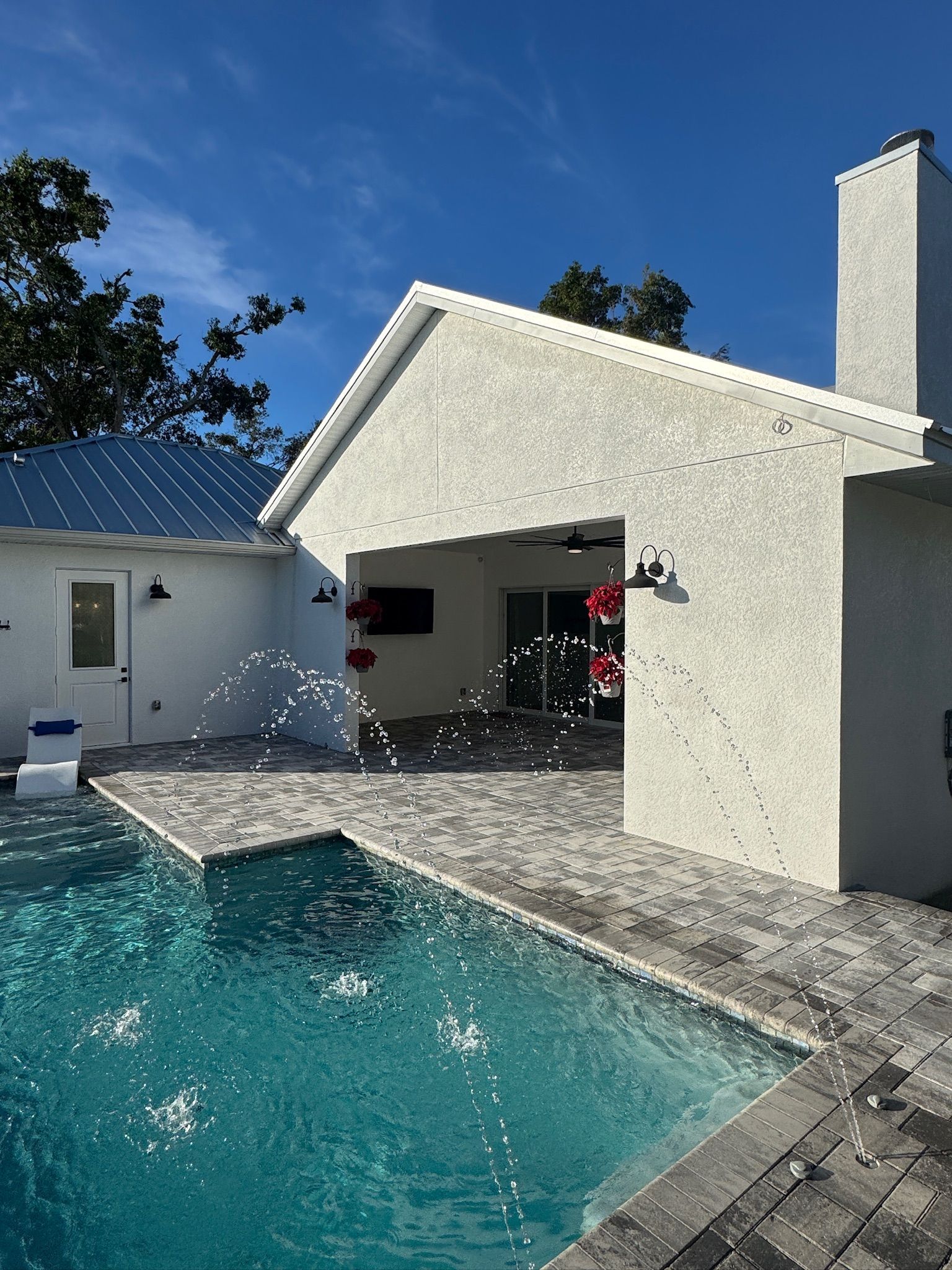 Backyard pool beside a white stucco house and patio under a clear blue sky