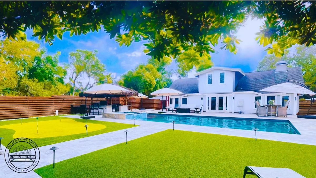 Bright backyard with a white house, turquoise pool, green lawn, and leafy trees under a blue sky.