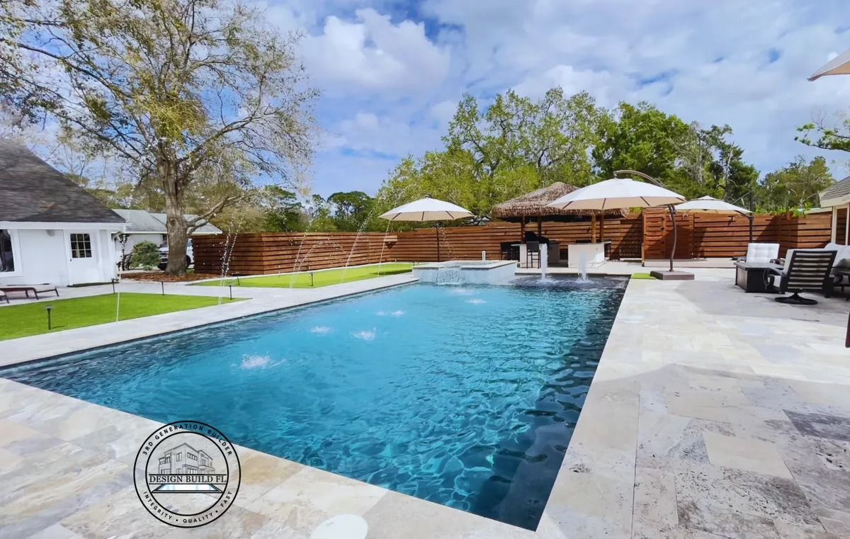 Rectangular outdoor swimming pool with blue water, lounge chairs, umbrellas, and a wooden deck under a bright sky