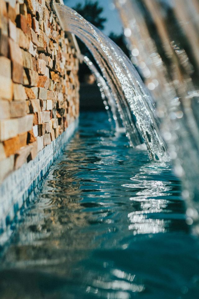Close-up of water streams pouring into a blue pool beside a stone wall