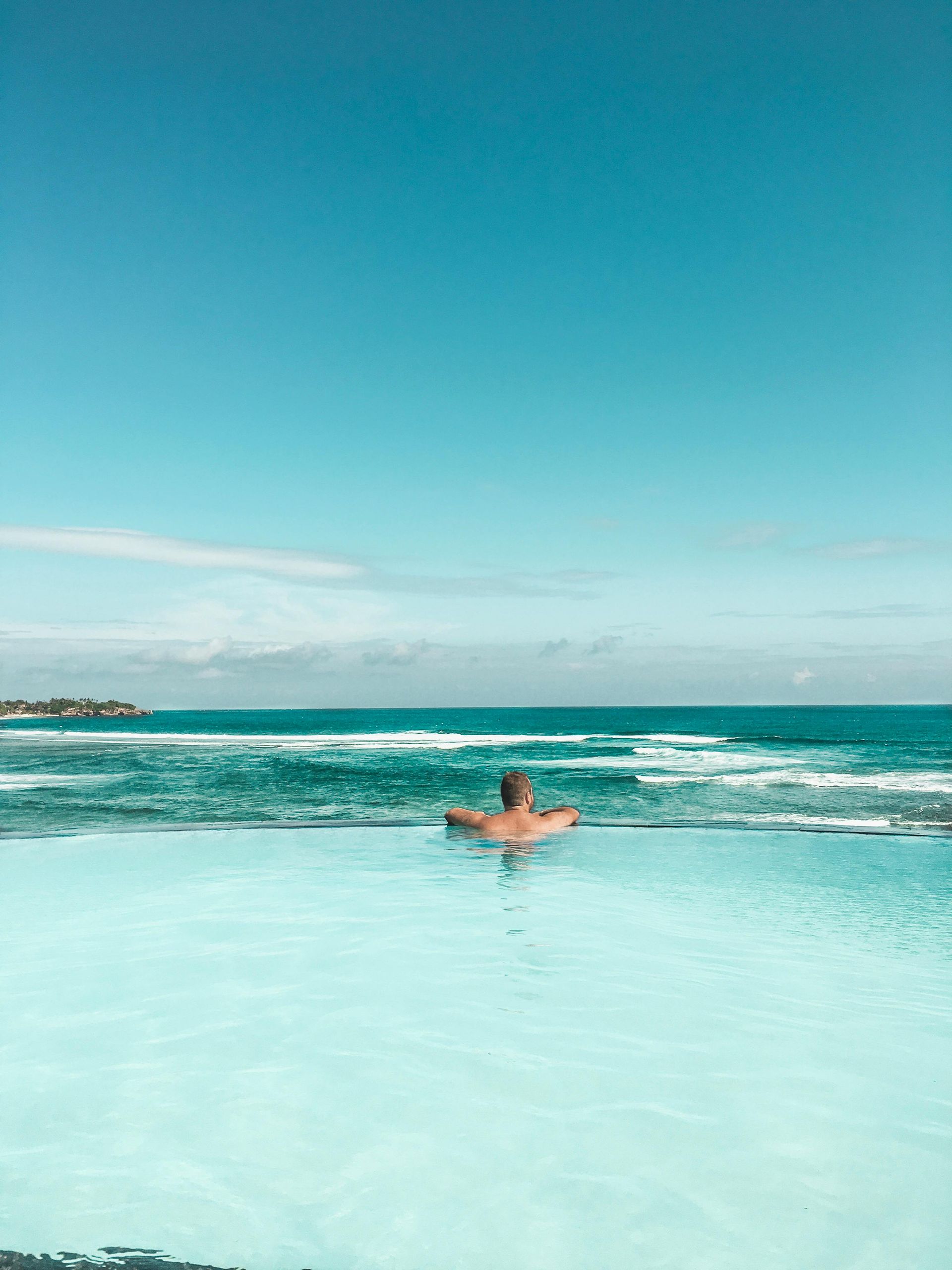 Person swimming in a turquoise ocean, floating near the shoreline under a clear blue sky
