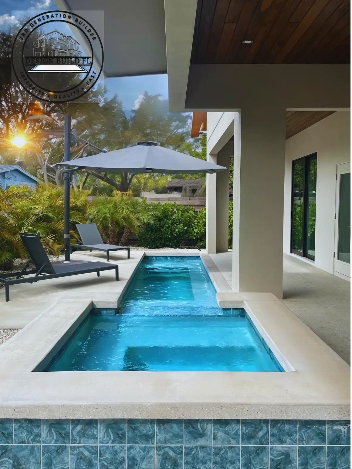 Modern patio with a turquoise swimming pool, lounge chairs, umbrella, and glass doors beside a home