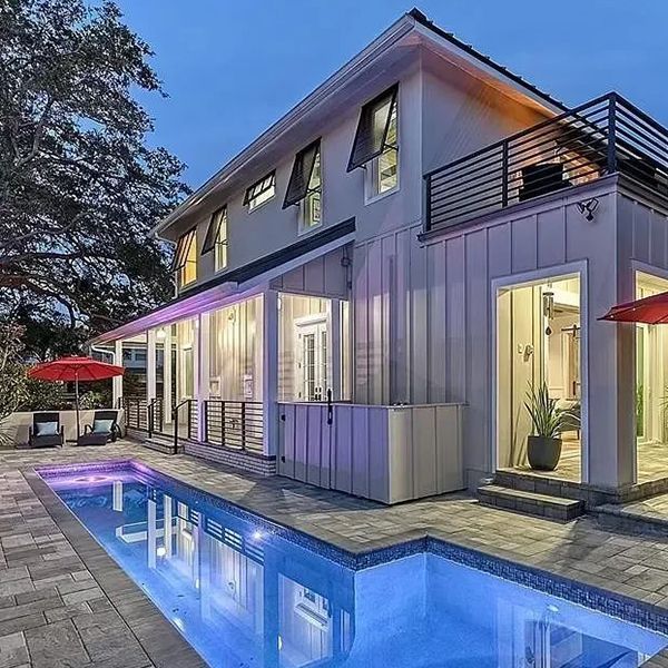 Modern two-story white house with lit pool and patio at dusk