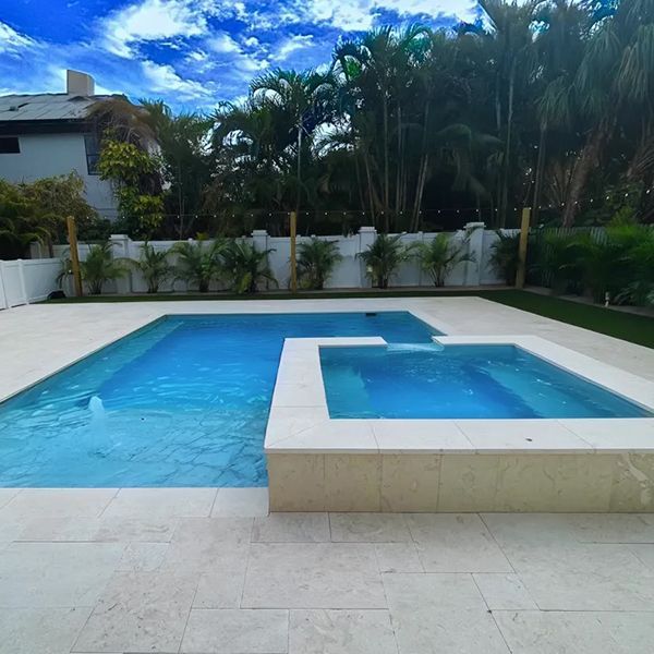 Backyard swimming pool with a shallow square spa and white tile deck, bordered by palm trees and greenery
