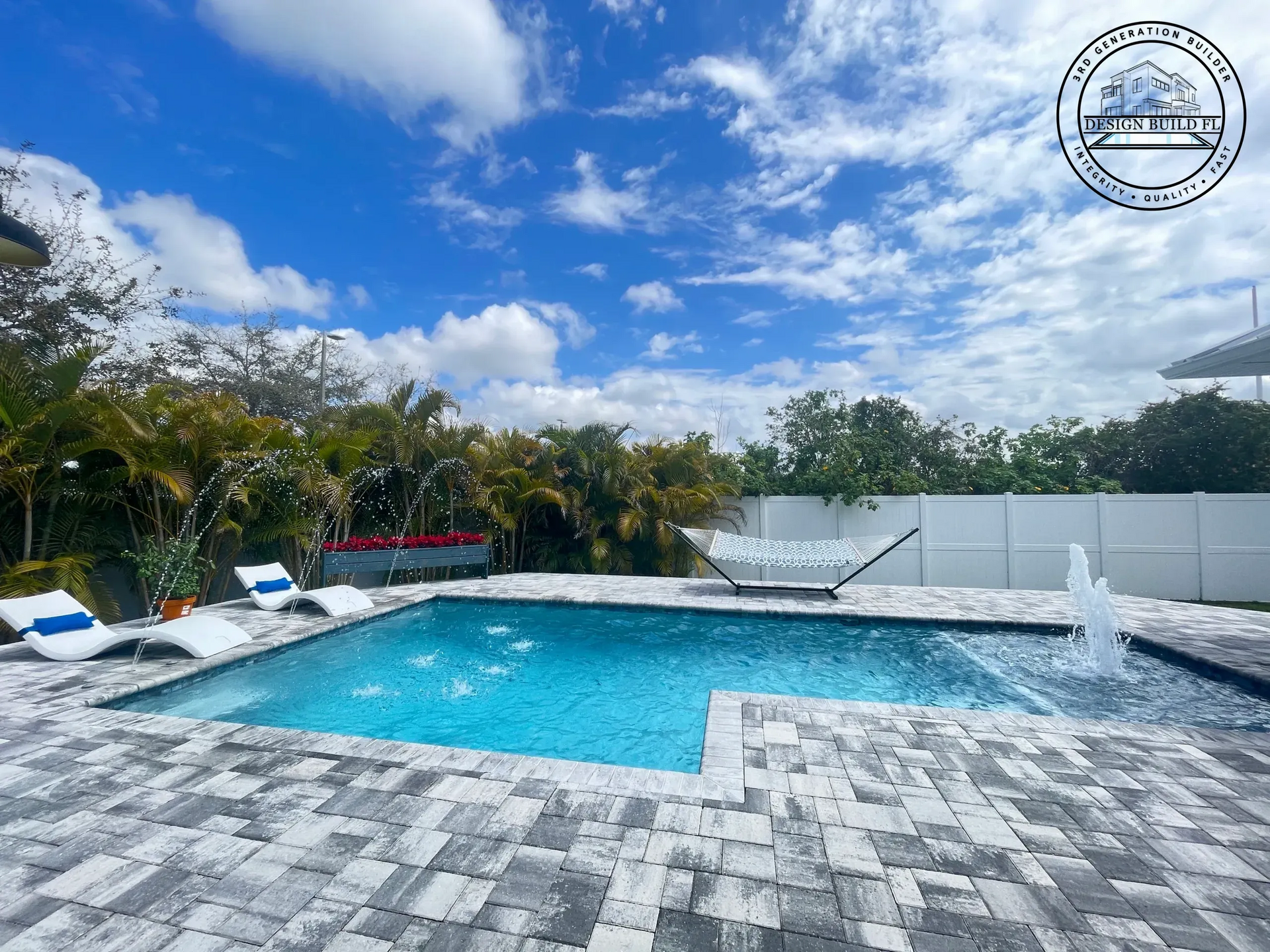 Backyard pool with shallow ledge, white tile deck, and palm trees under a blue sky