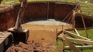 Excavator bucket dumping dirt into a large rust-colored metal pit on a construction site