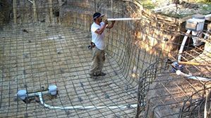Worker bending rebar cage at a construction site inside a dug-out foundation pit