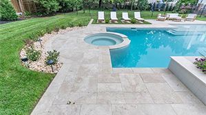Backyard pool with stone patio, circular spa, and lounge chairs by landscaped lawn