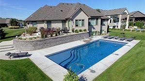Backyard swimming pool beside a modern house with patio and landscaped lawn