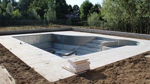 Empty in-ground swimming pool under construction with a concrete deck and stacked materials nearby