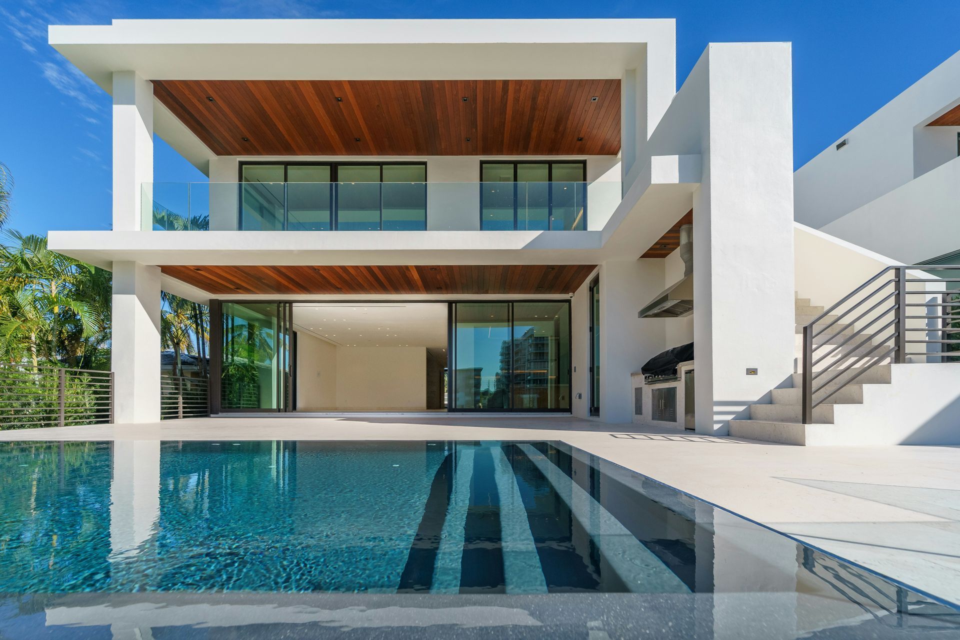 Modern white luxury villa with large pool and glass walls under a blue sky