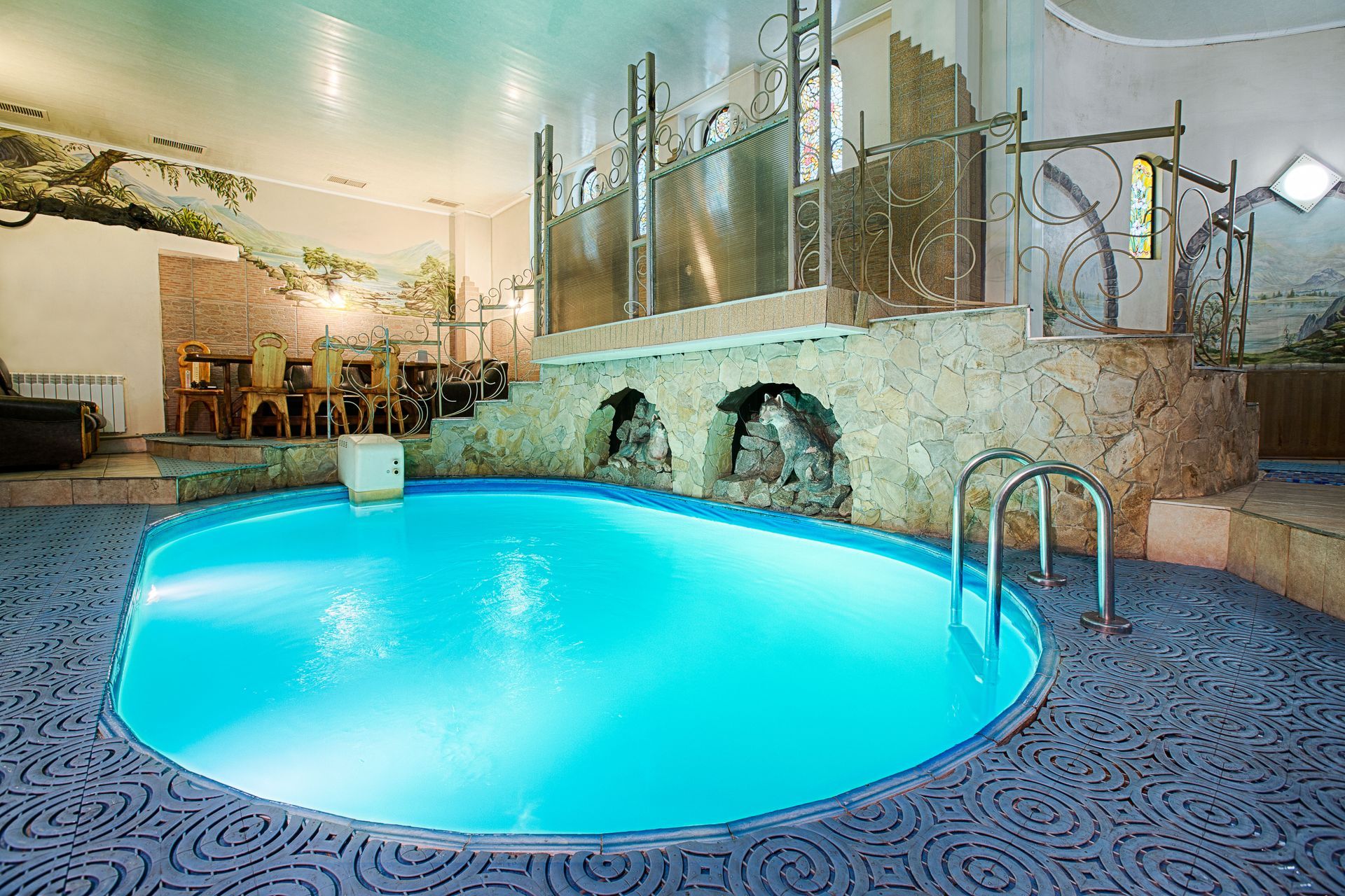 Indoor spa pool with glowing blue water, stone waterfall wall, and lounge seating