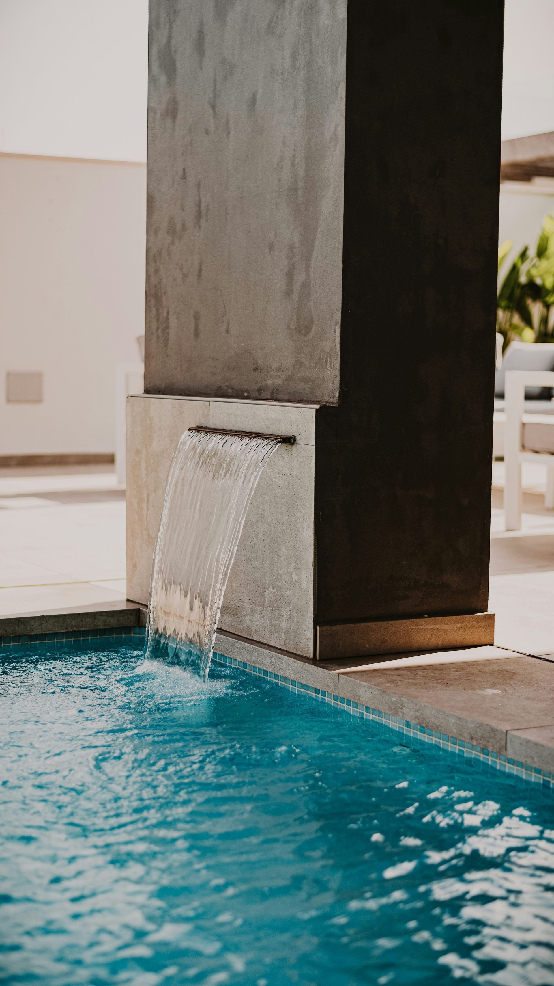 Modern pool with a concrete pillar waterfall spilling into clear blue water