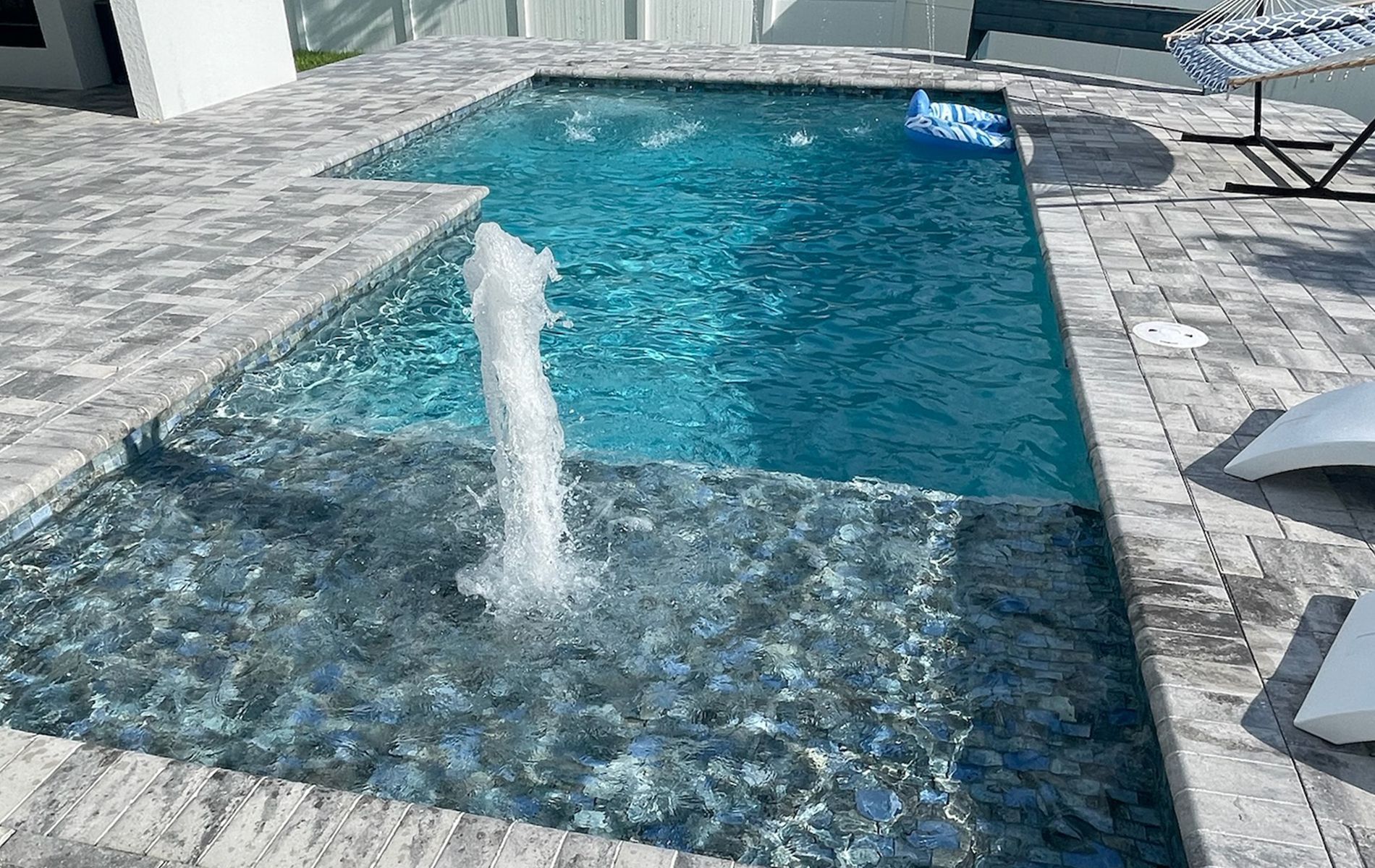 Backyard pool with a raised spa and fountain, surrounded by stone decking and lounge chairs