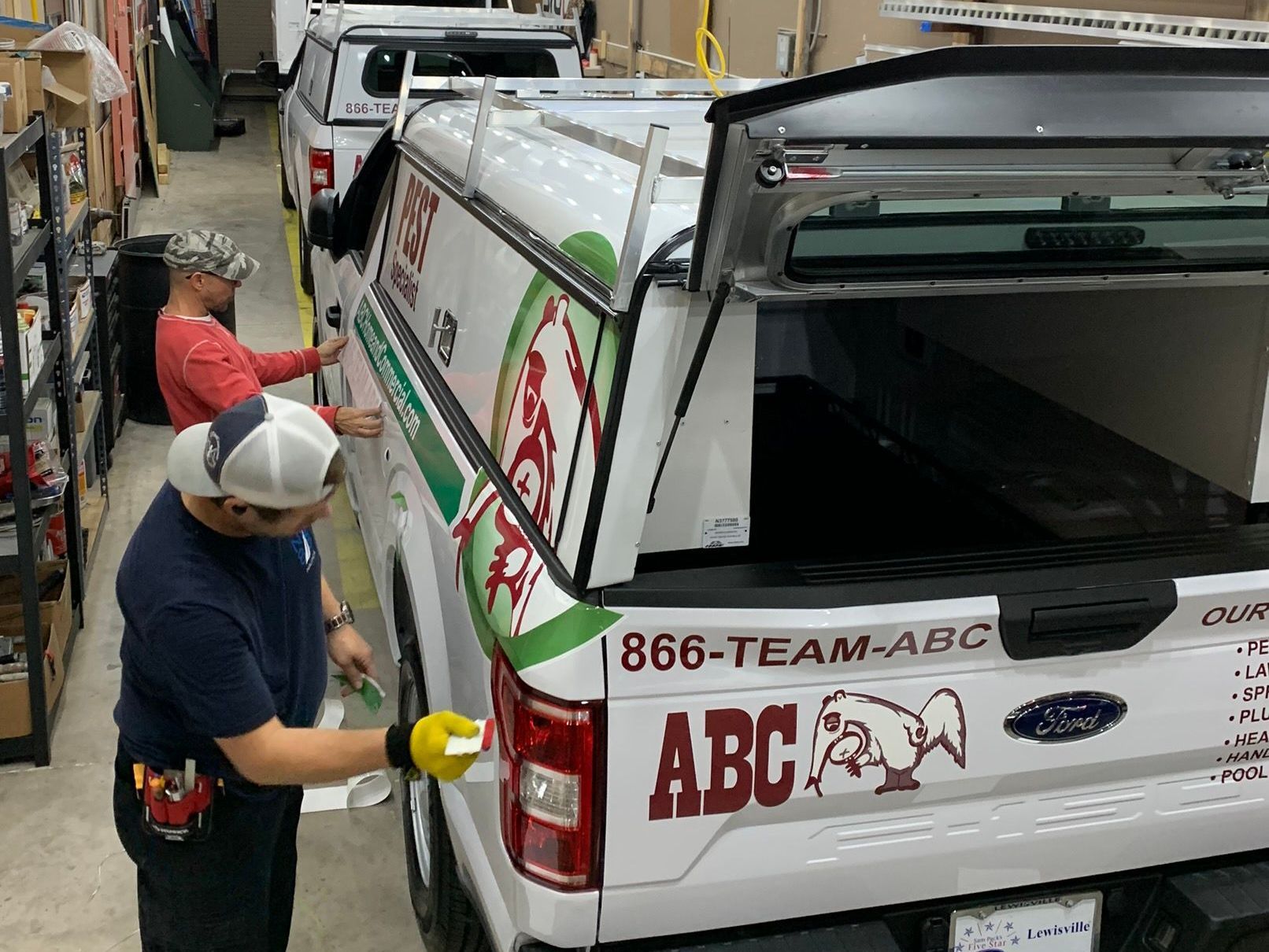 Vehicle graphics being installed in commercial install bay on fleet trucks for commercial pest control company.