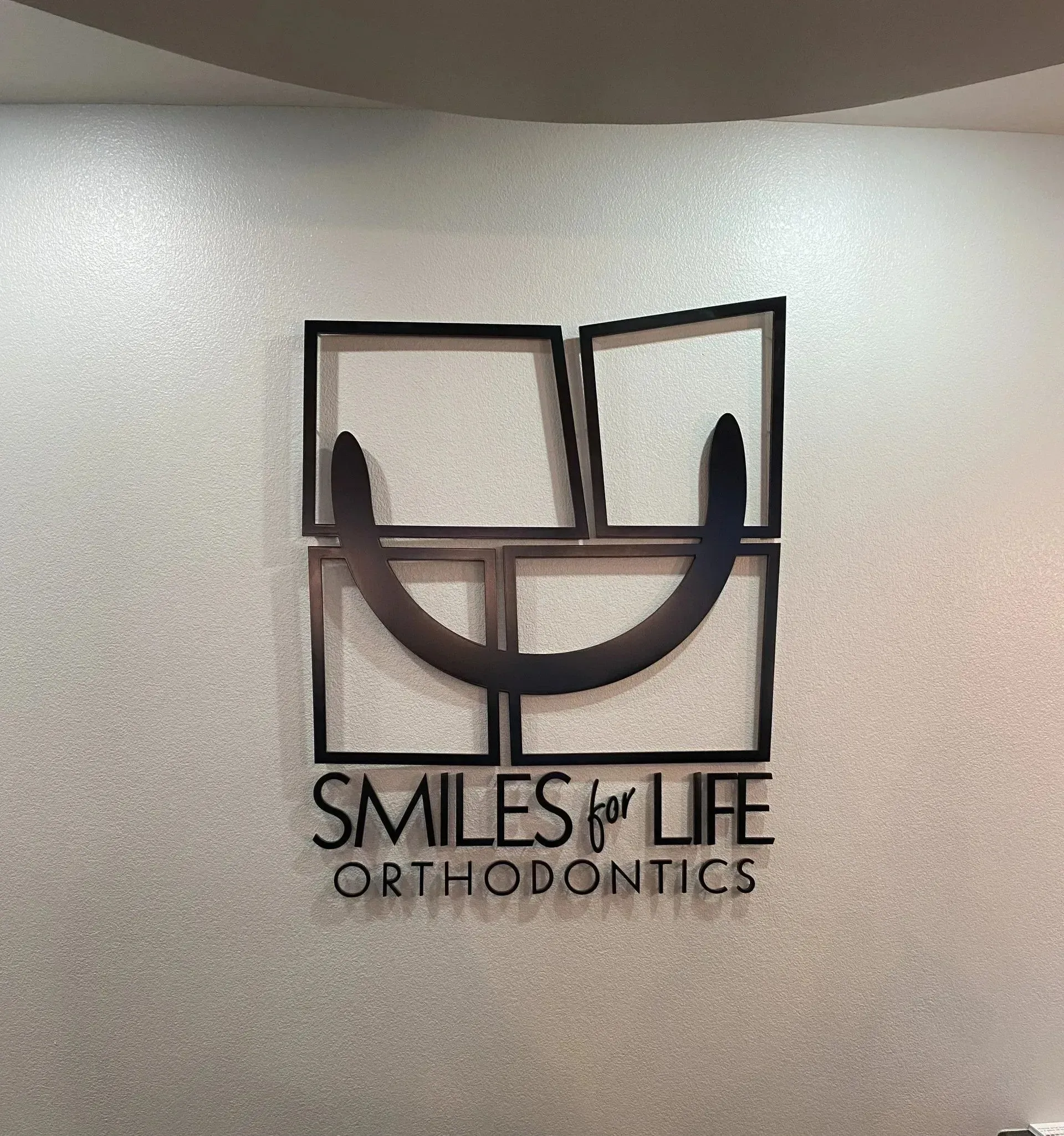 Dimensional aluminum logo stud mounted on interior wall for Smiles for Life Orthodontics in Lewisville, TX