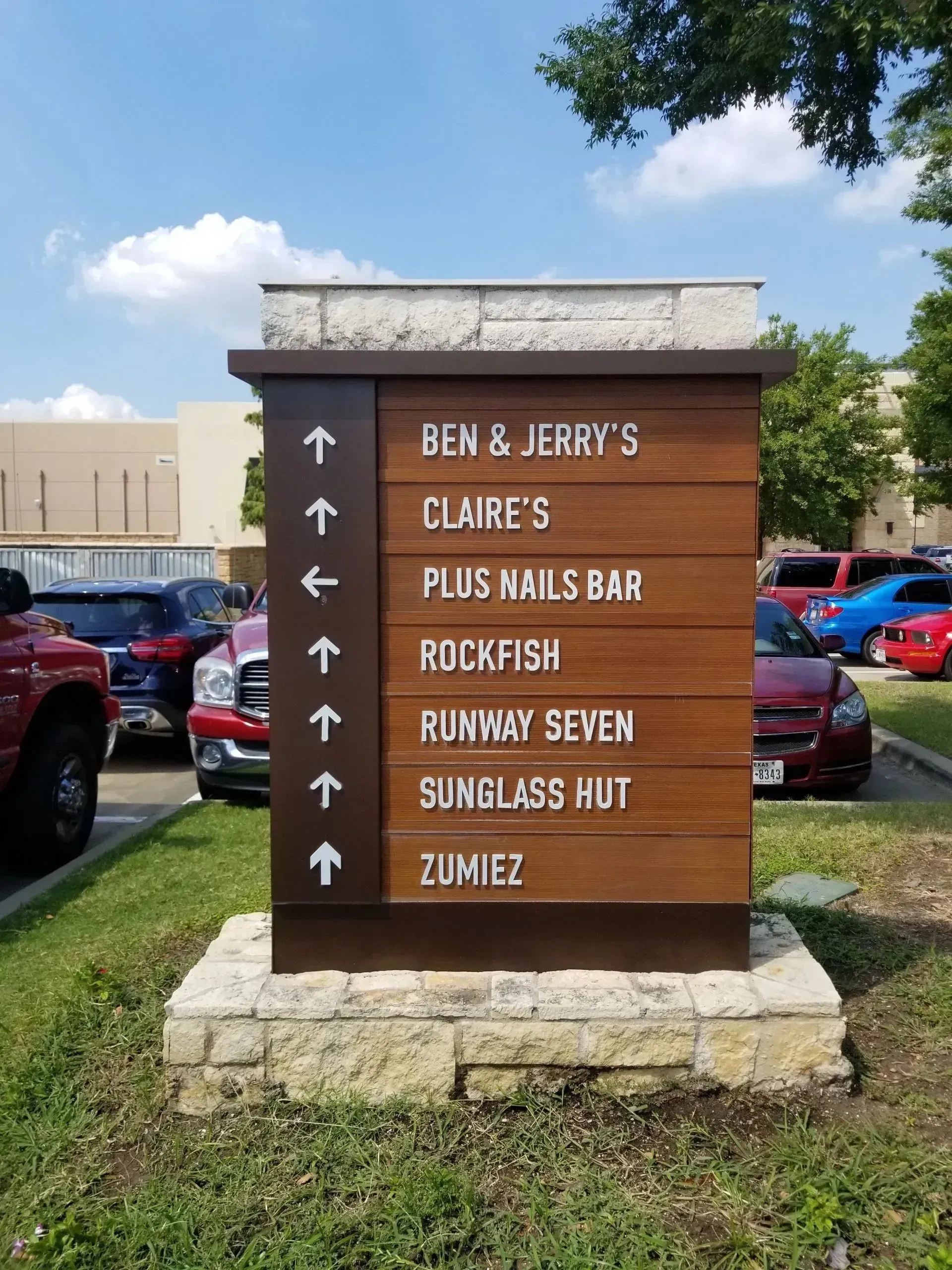 Wayfinding directory sign fabricated metal with acrylic lettering on wood grain powder coated panels Austin stone base and topper at Shops at Highland Village development.