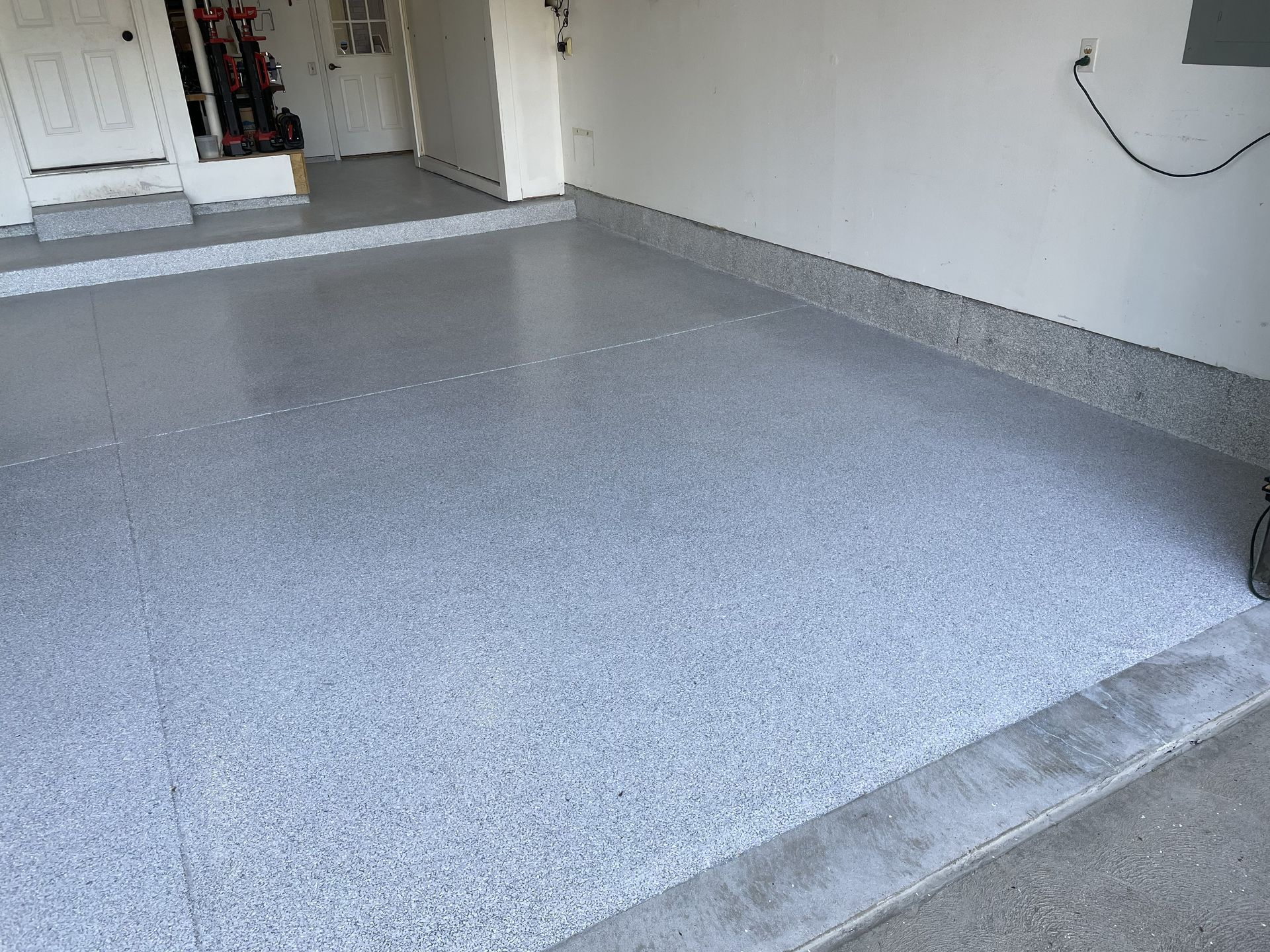 Grey speckled epoxy floor in a garage with white walls and a door in the background.