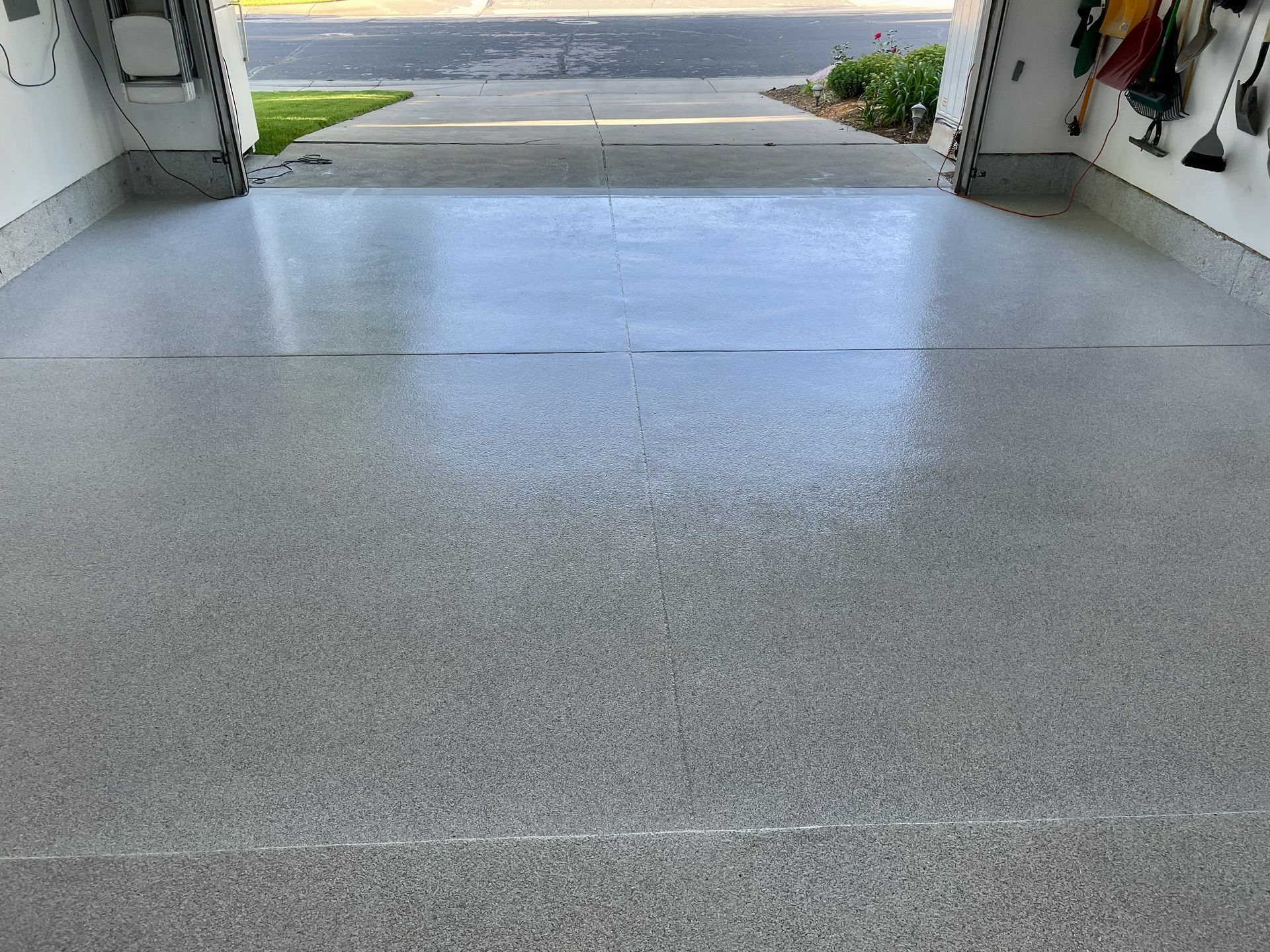 Grey epoxy-coated garage floor with open door to driveway and greenery.