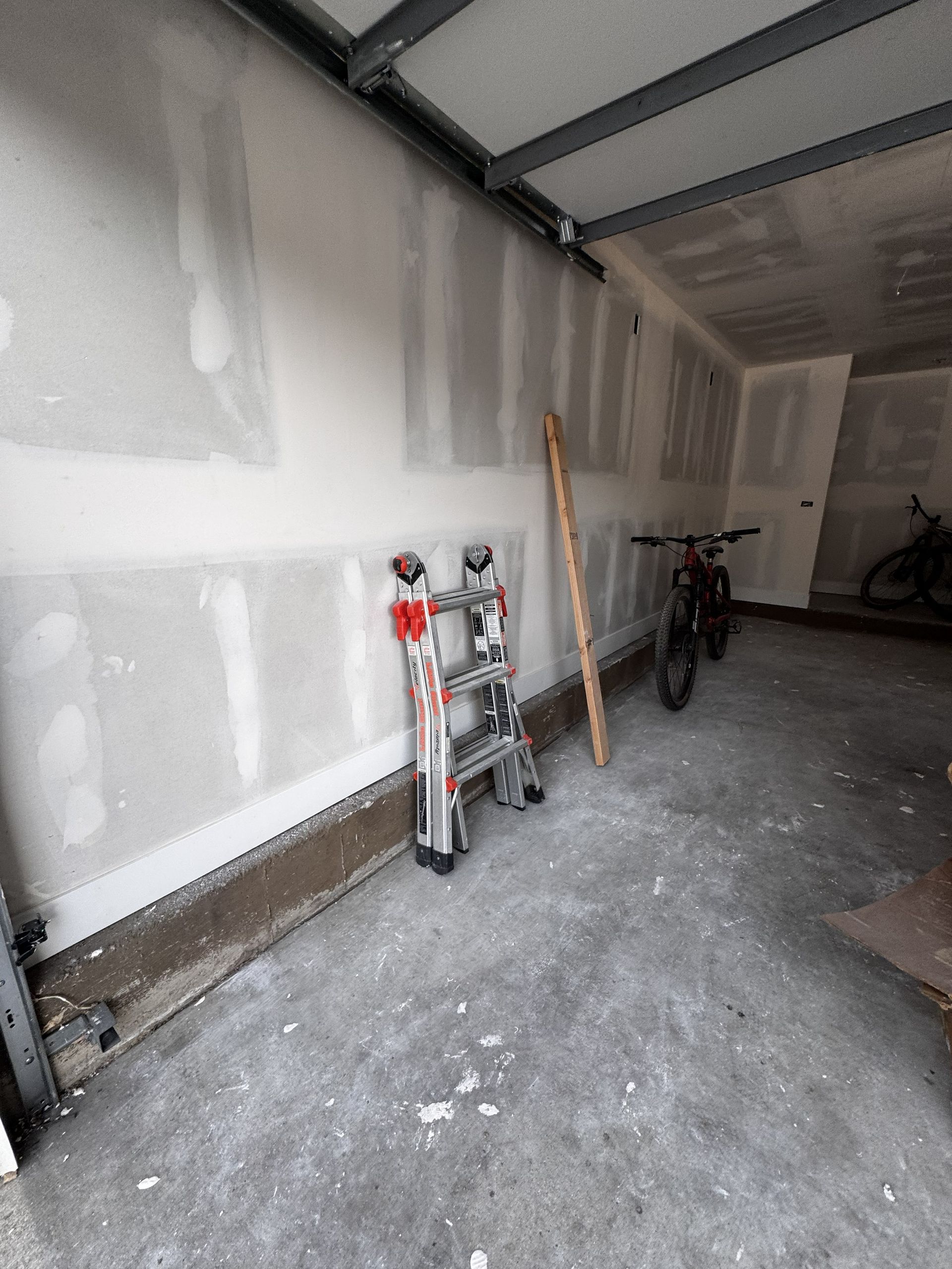 Garage interior with drywall on the walls, ladder, bike, and wood beam. Concrete floor.
