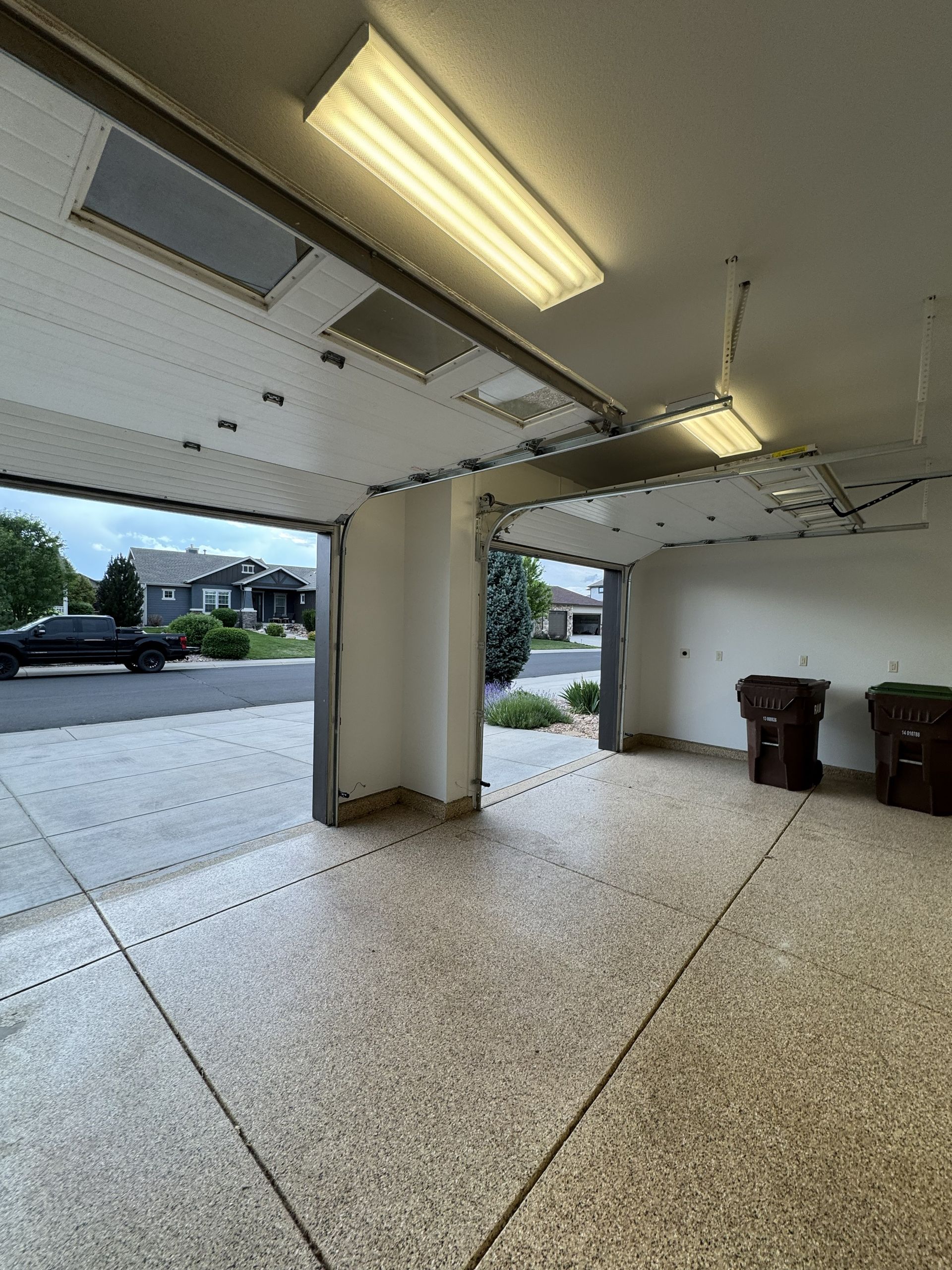 Open garage with epoxy floor, open to the street. Fluorescent lights illuminate the interior.