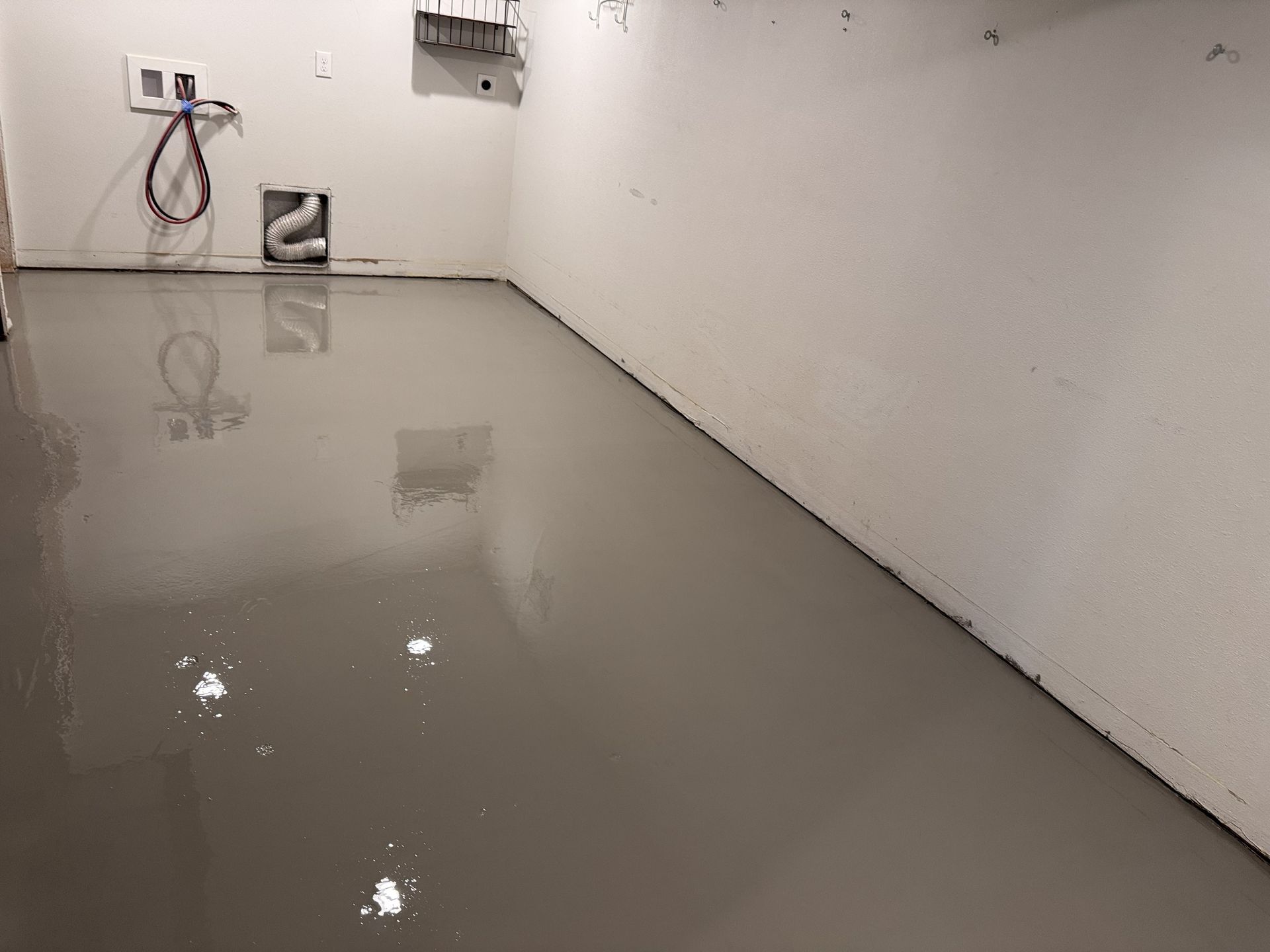 Gray epoxy-coated floor in an empty room with white walls. Electrical and plumbing fixtures visible.