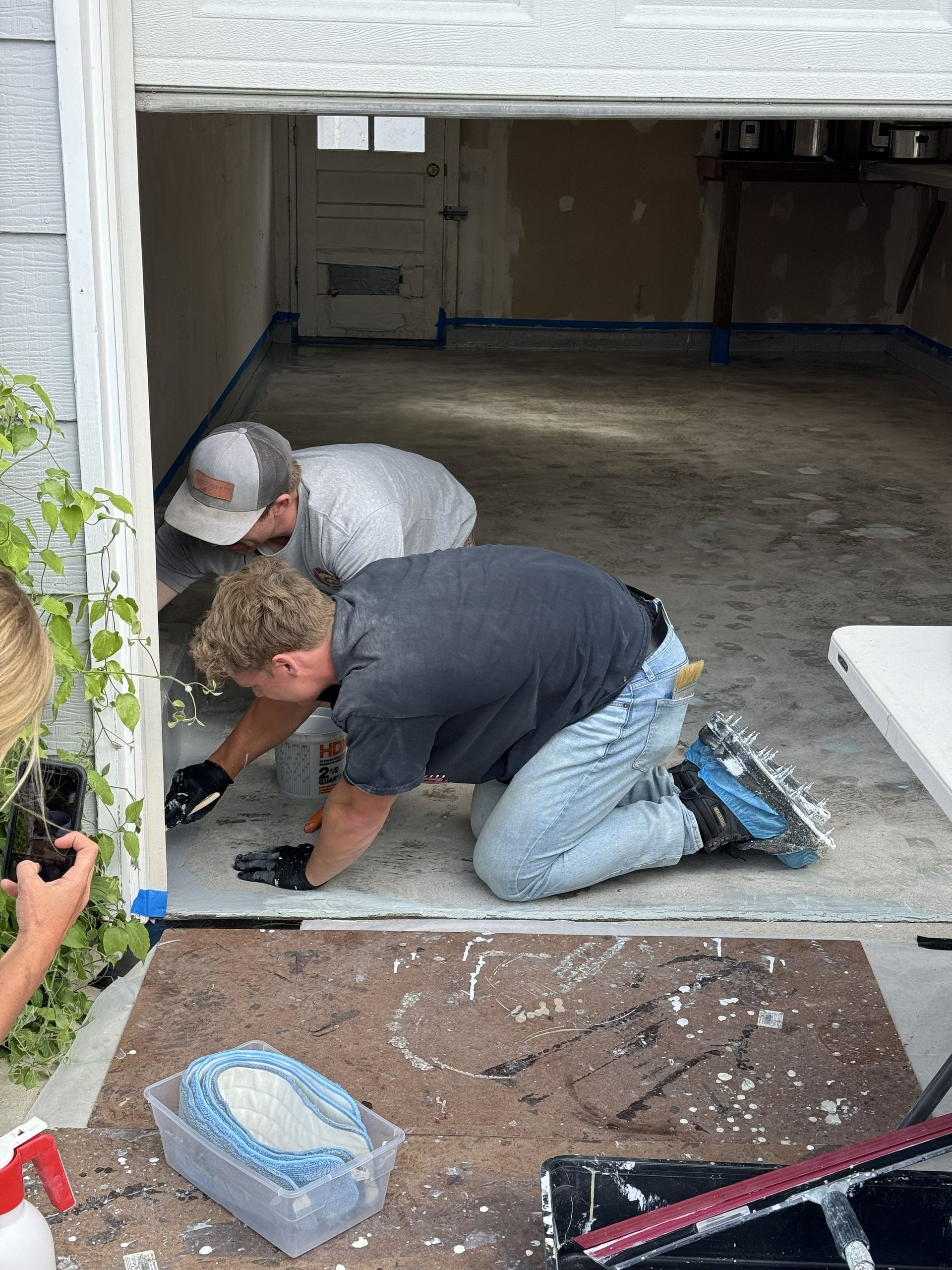 Two people preparing a garage for painting, kneeling and taping edges.