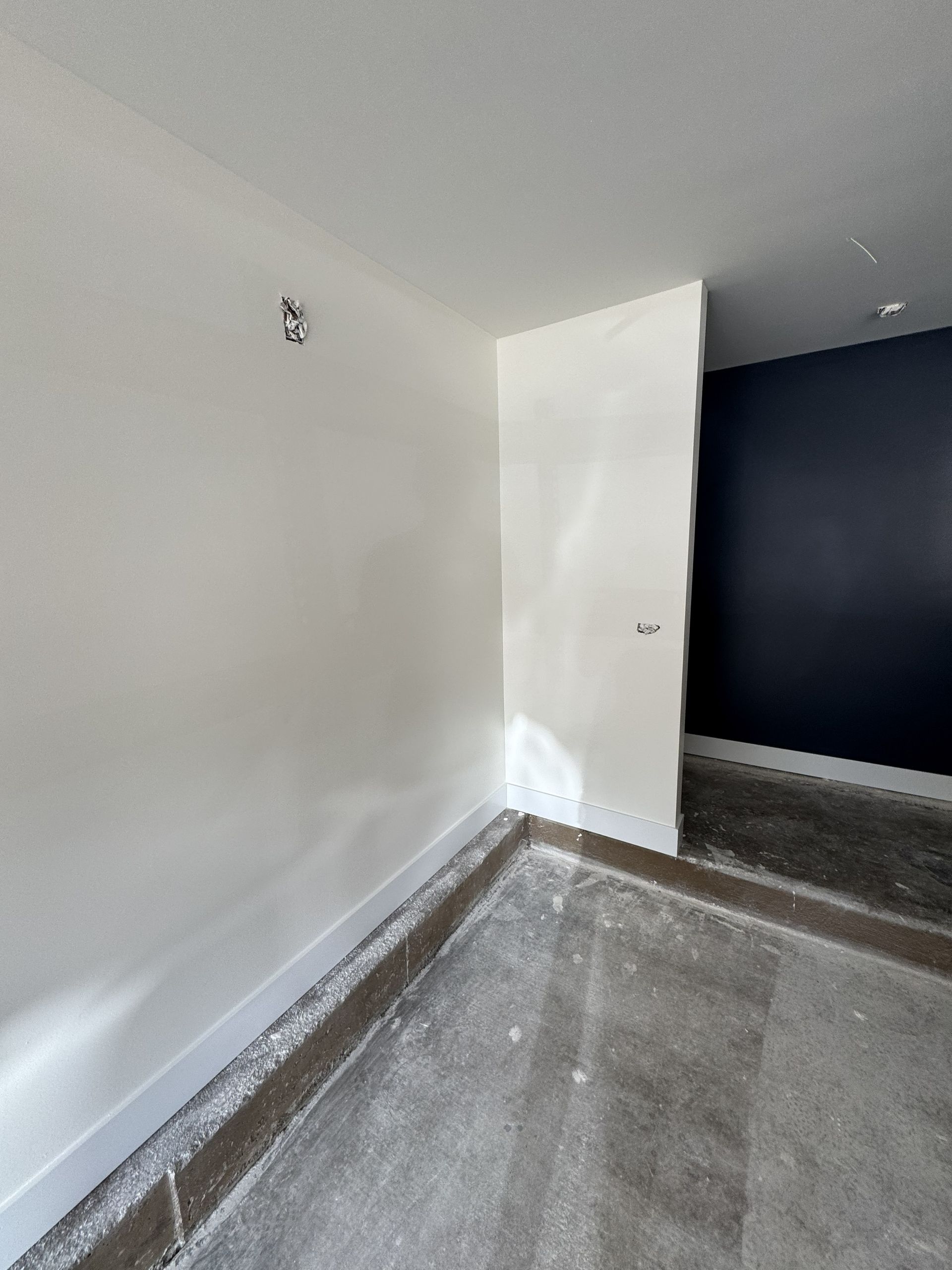 Interior corner of a room, with white walls, unfinished concrete floor, and dark blue accent wall.