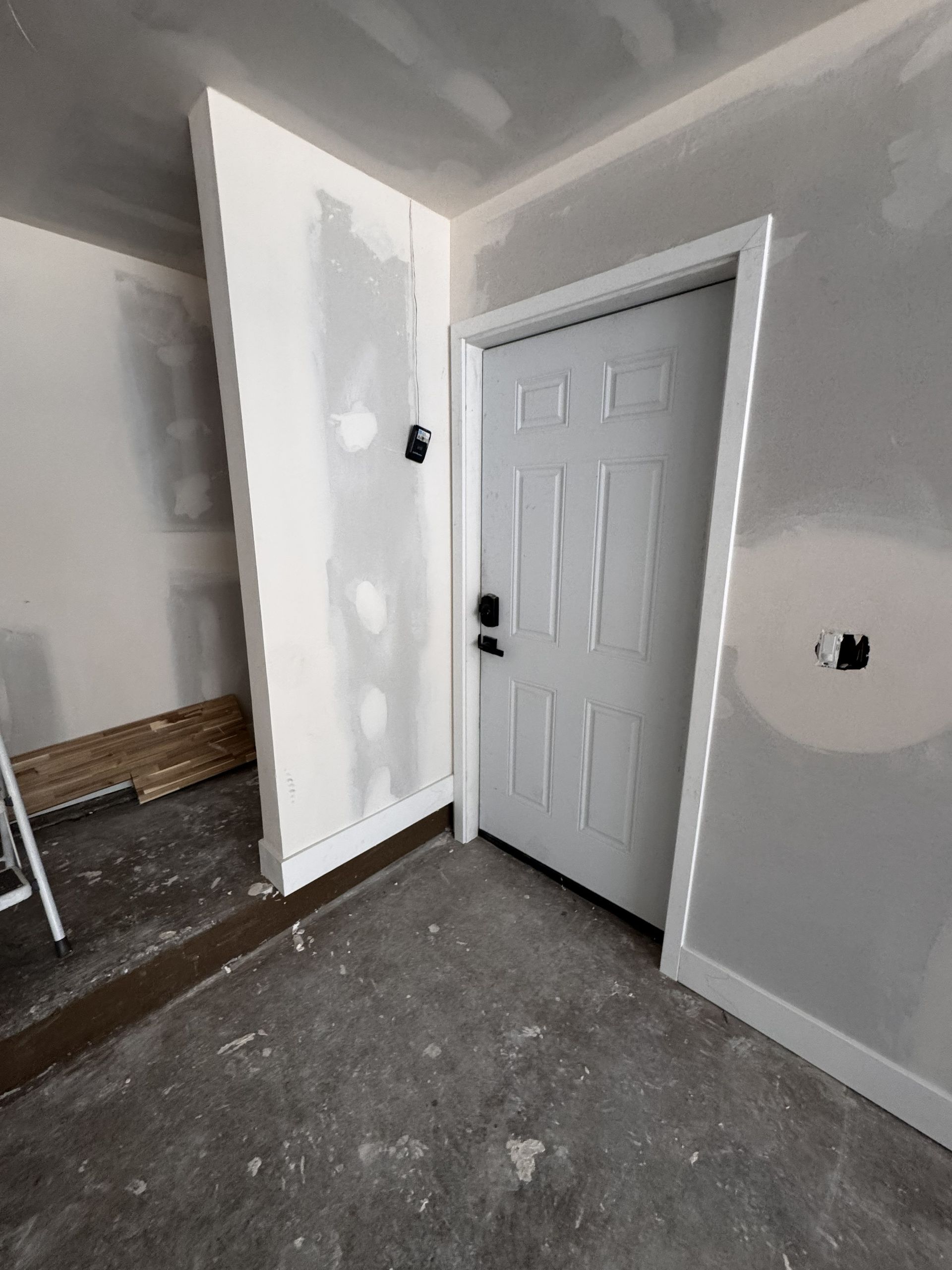 White door in a room under construction with unfinished walls and flooring.