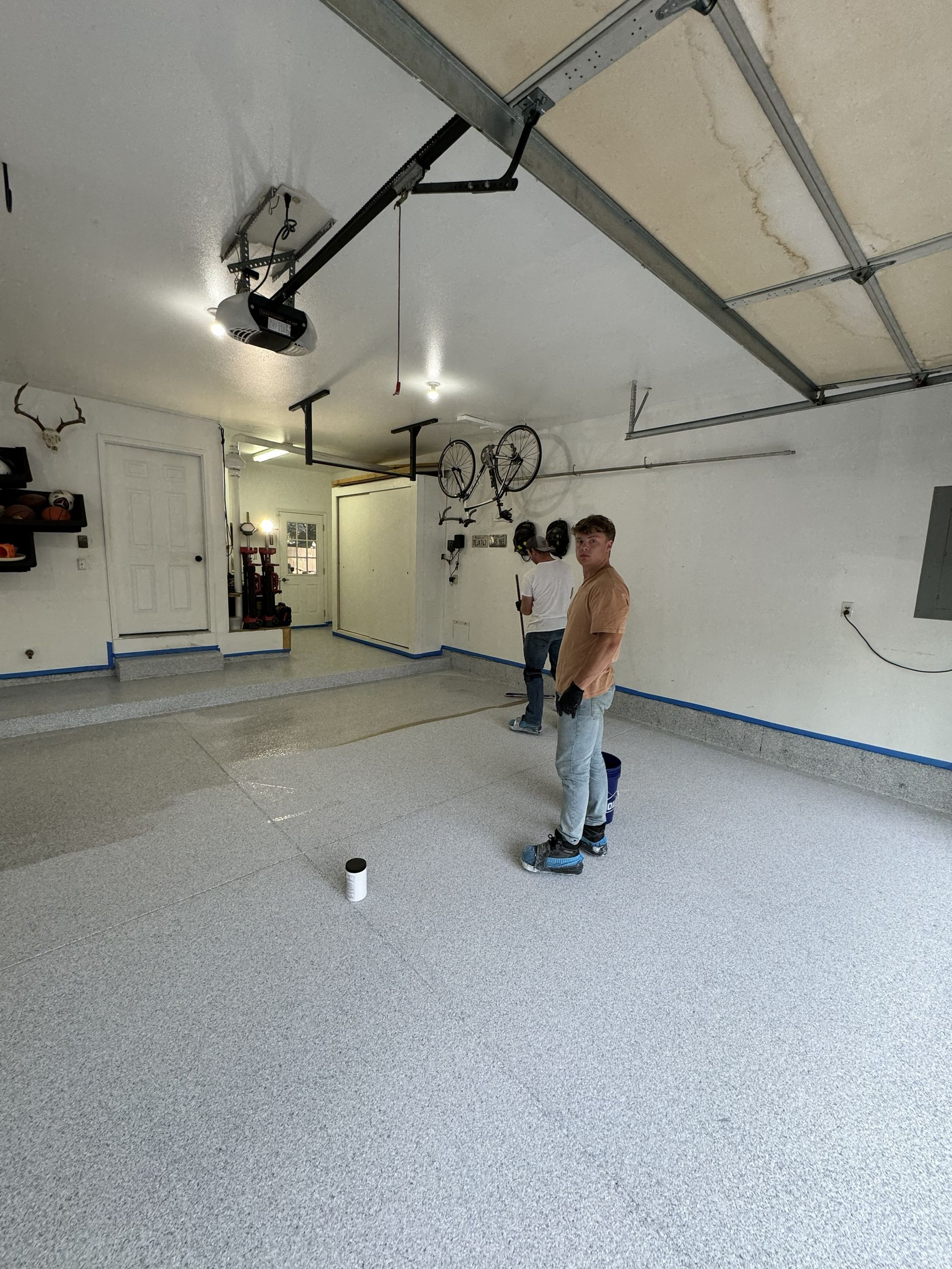 Two people inside a garage with a speckled epoxy floor. One holds a roller, other with paint.