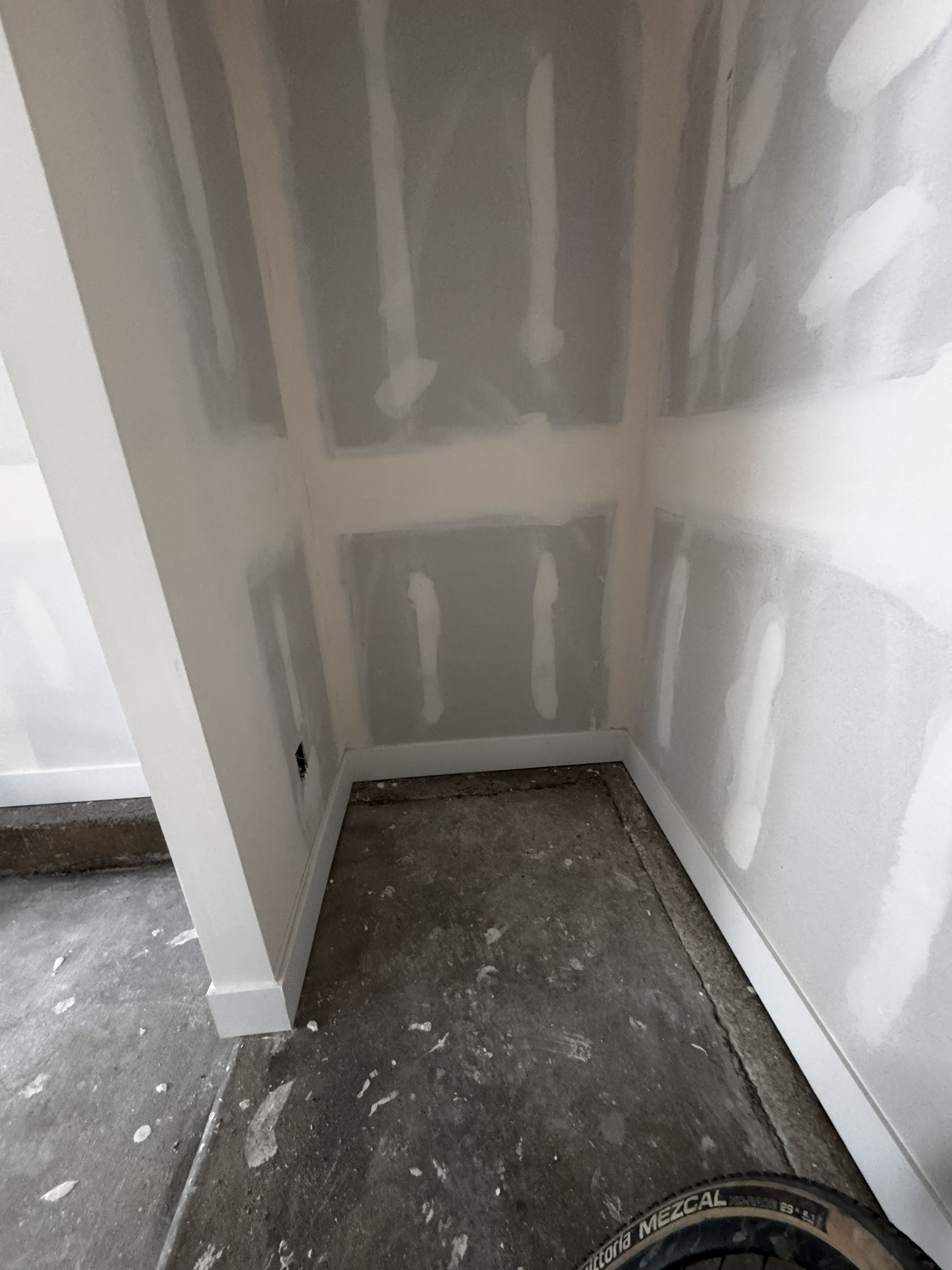 Unfinished interior room with drywall walls and concrete floor. White trim along edges.