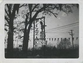 A black and white photo of a pizza king sign surrounded by trees.