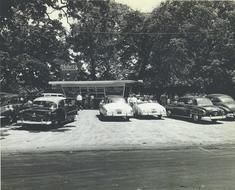 A black and white photo of a parking lot with cars parked in front of a building.